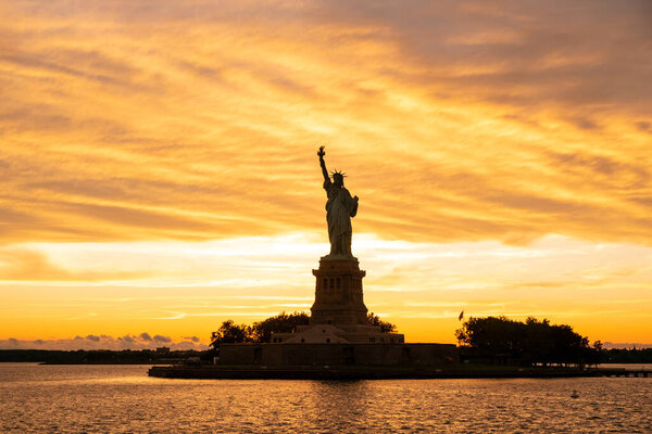 The Statue of Liberty at New York city during sunset with reflections on the ocean