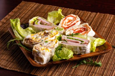 Somon, ton balığı, jambon, yumurta ve yeşil sebzelerle dilimlenmiş yumurta ruloları bambu hasırında ahşap tabakta.. 