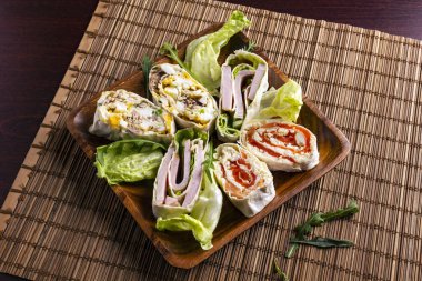 Somon, ton balığı, jambon, yumurta ve yeşil sebzelerle dilimlenmiş yumurta ruloları bambu hasırında. Üst görünüm.