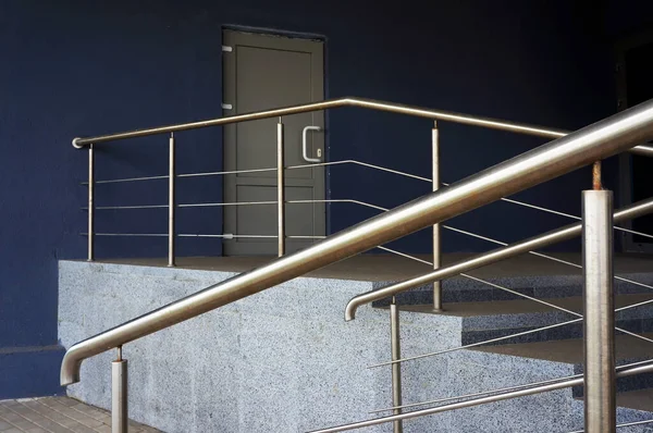 Porch steps and metal railing in front of closed door of entrance in modern building.