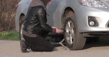 Arabanın tekerleğini değiştirmek, yol kenarında yedek lastik, vidaları sökmek, araba tamir sorunu.