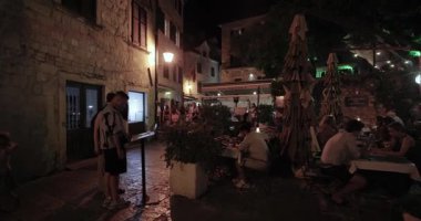 Kotor, Karadağ - 26 Temmuz 2024: Kotor 'un eski ortaçağ şehir merkezinde yürümek, muhteşem taş bina mimarisi ve kaldırım caddeleri ile turizm beldesi, geceleri bir meydanda restoran