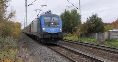 Ecser, Macaristan - 21 Ekim 2025: Uluslararası tren durmadan geçen küçük bir demiryolunda elektrikli yolcu treni