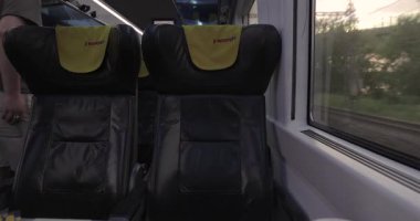 Pardubice, Çek Cumhuriyeti - 2 Haziran 2025: Çek özel demiryolu şirketi Regiojet ile gün batımında seyahat eden tren yolculuğu penceresi manzarası ve ücretsiz koltuklar. Konteyner yük treni geçiyor.