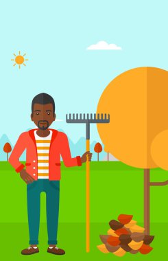 Man with rake near tree and heap of leaves.