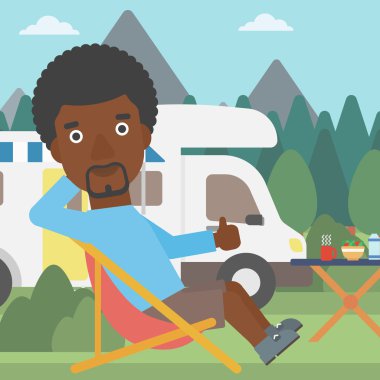 Camper van önünde sandalyede oturan adam.