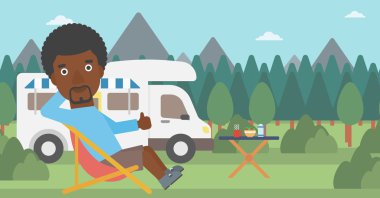 Camper van önünde sandalyede oturan adam.