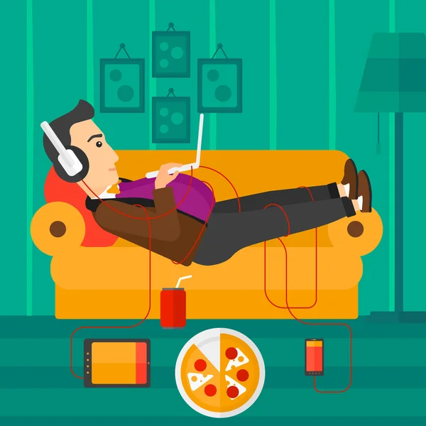 Uomo sdraiato sul divano con molti gadget . — Vettoriale Stock