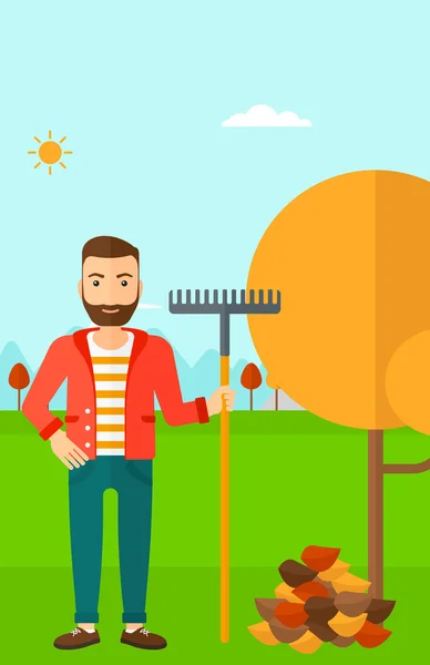 Man with rake standing near tree and heap of autumn leaves. — Stock Vector