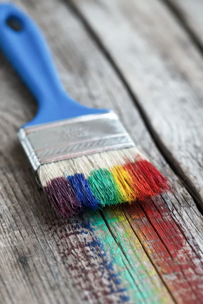 Penseel en multicolor regenboog penseelstreken op houten plank. — Stockfoto