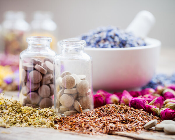 Bottles of tablets, healing herbs and mortar with dry lavender