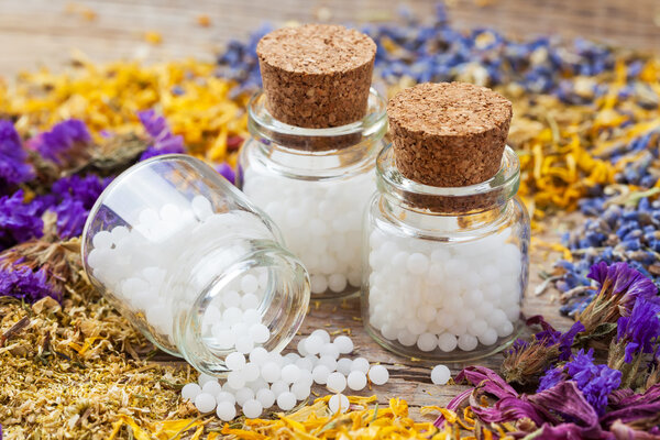 Bottles of homeopathy globules and dry healthy herbs on table.