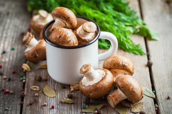 Cogumelos em caneca esmaltada branca, endro e especiarias na mesa de madeira — Fotografia de Stock