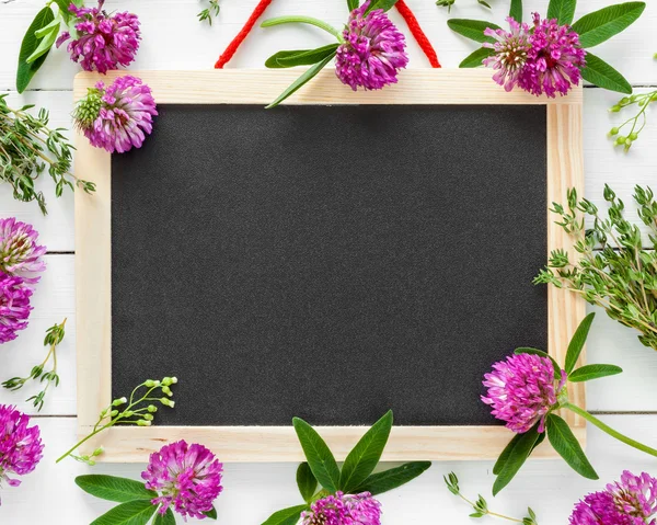 Empty blackboard, floral border from flowers and herbs. Top view — Stock Photo, Image