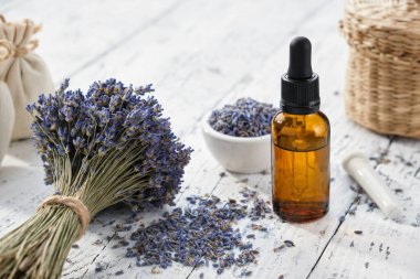 Bir şişe lavanta yağı, kese poşetleri ve beyaz ahşap masa üzerinde kurutulmuş lavanta çiçekleri.. 