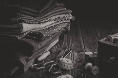 Dikiş, makas, mezura, iplik makarası, ahşap aksesuar kutusu için kumaş yığını. Siyah beyaz fotoğraf..