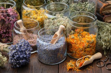 Glass jars of dry lavender and calendula flowers. Jars of dry medicinal herbs for making herbal tea, bunch of dry lavender on table. Alternative medicine. clipart