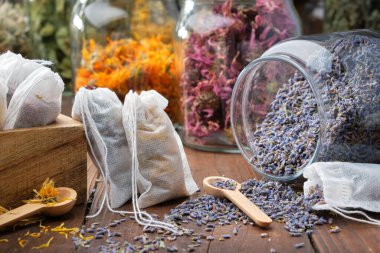 Şifalı bitkilerle dolu çay poşetlerini filtrele. Bitki çayı yapmak için bir kavanoz kuru lavanta çiçeği ve arka planda çeşitli sağlıklı otlar. Alternatif tıp.