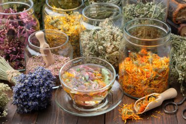 Bir bardak sağlıklı Calendula çayı, kurutulmuş şifalı otlar, funda, takvim, koni çiçekleri, Melissa, ıhlamur ağacı çiçekleri, ahşap masada bir demet kuru lavanta. Alternatif tıp.  