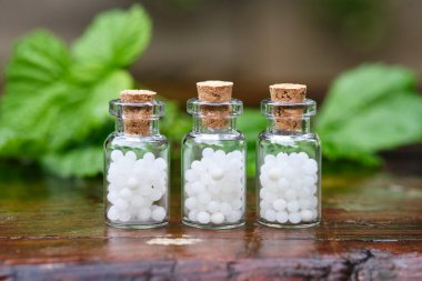 Three bottles of homeopathy globules. Bottles of homeopathic granules. Medicinal herbs on background. Homeopathy medicine concept. 