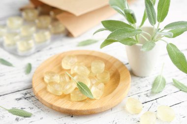 Boğaz ağrısı ve öksürük için tahta bir tabak adaçayı pastili. Beyaz ahşap masaya adaçayı ya da salvia resmi çiçekleri..