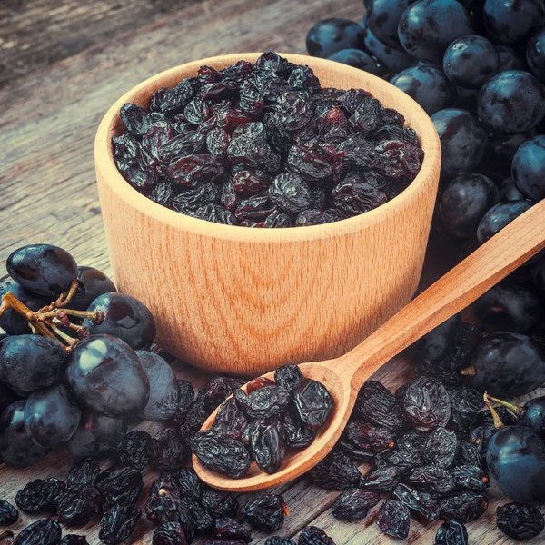 Rozijnen in kom en blauwe druiven op tafel — Stockfoto