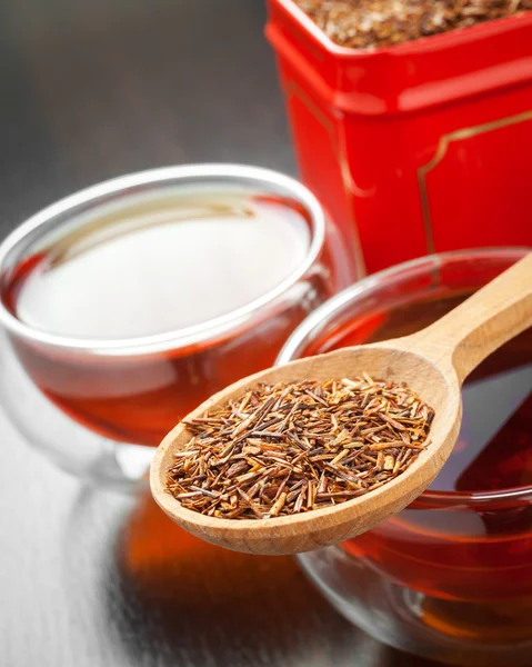 Rooibos in wooden spoon closeup, two tea cups and tea tin box — Stock Photo, Image