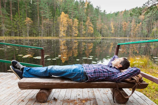 Mladý muž tramp odpočívá nedaleko jezera v podzimním lese — Stock fotografie