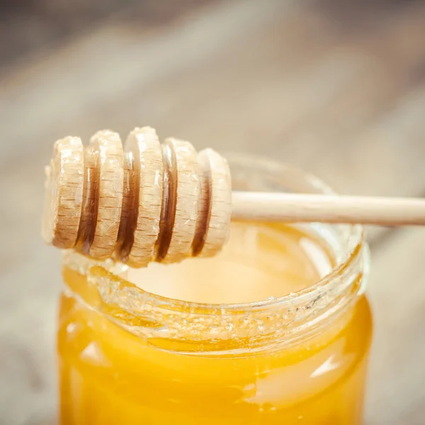 Honey in glass jar and wooden dipper — Stock Photo, Image