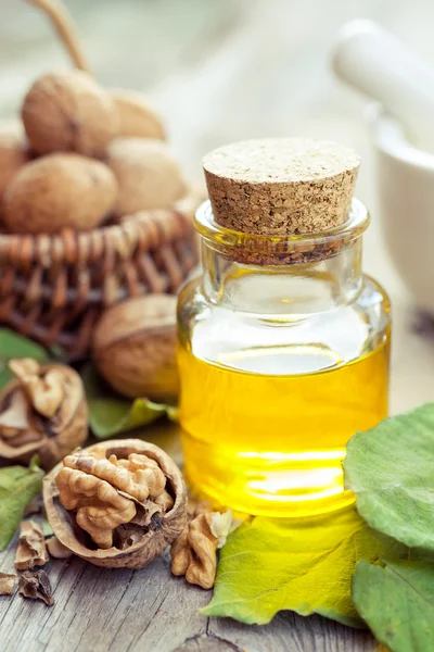 Walnuts, bottle of essential oil and basket with nuts on old kit — Stock Photo, Image