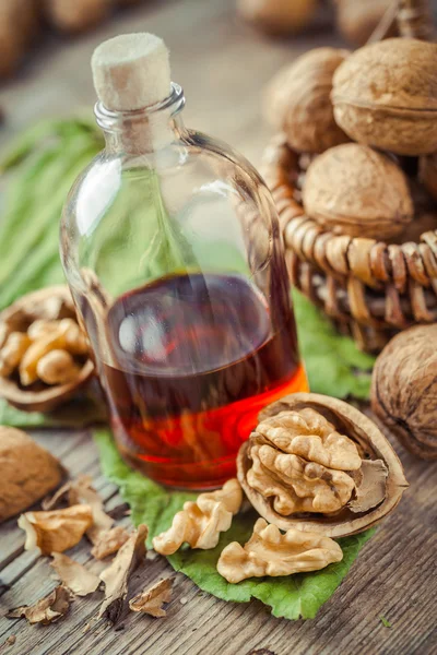Walnuts, bottle of tincture or oil and wicker basket with nuts o — Stock Photo, Image