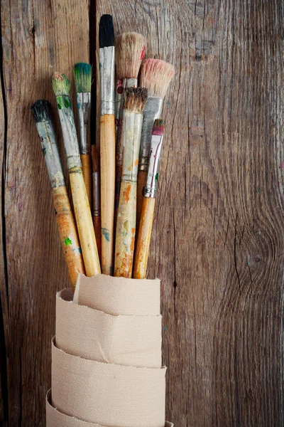 Artist paintbrushes and roll of canvas on wooden background — Stock Photo, Image