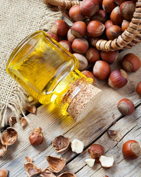 Sebotol minyak kacang dan keranjang dengan hazelnut di meja dapur tua — Stok Foto