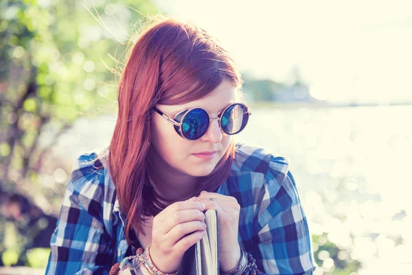 Pensive beautiful young woman in sunglasses with book near river — Stock Photo, Image
