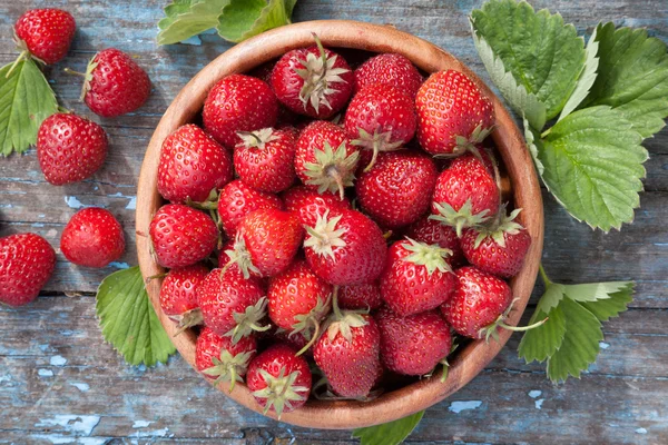 Reife Erdbeeren in Holzschale und grüne Blätter auf altem Tisch, — Stockfoto