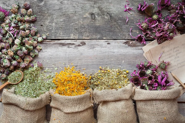 Erbe curative in sacchetti di iuta su vecchio tavolo rustico in legno, erbe aromatiche — Foto Stock