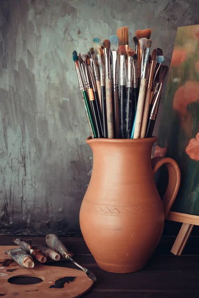 Pincéis em um jarro de oleiros argila, paleta, tubos de pintura e — Fotografia de Stock