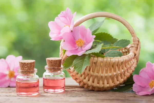 Рустикальний плетений кошик з квітами рожевого стегна та пляшками есе — стокове фото