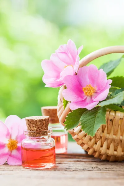 Cesta de mimbre rústica con flores de rosa mosqueta y botellas de esencia — Foto de Stock