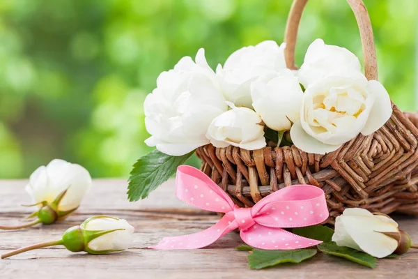 Rustic wicker basket with wild rose flowers and pink ribbon. — Stock Photo, Image