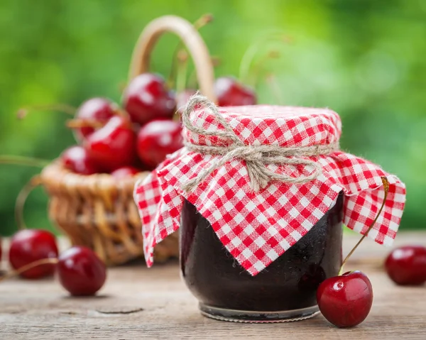Jars of jam and basket with cherry on background. — Stockfoto