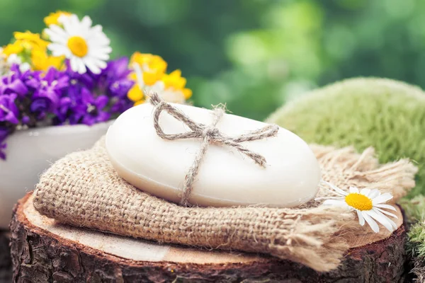 Soap on rustic stump. Flowers and moss on background. — Stock Photo, Image