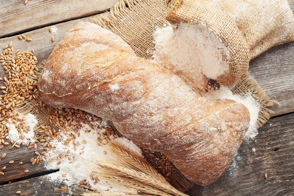 Pane fresco fatto in casa, sacco di farina e spighe di grano su corteggiamento rustico — Foto Stock