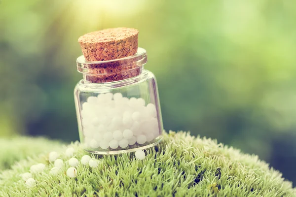 Bottle of homeopathy globules on green moss. Retro styled. — Stock Photo, Image