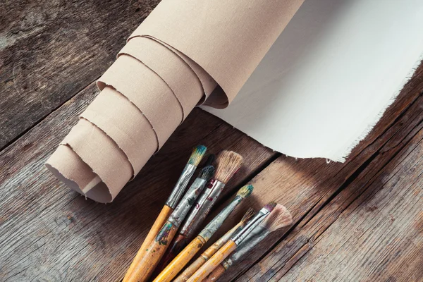 Artist canvas in roll and paintbrushes on old rustic table — Stock Photo, Image