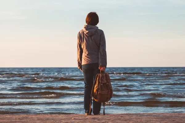 Unga turist kvinna med ryggsäck ser att havet i solnedgången. — Stockfoto