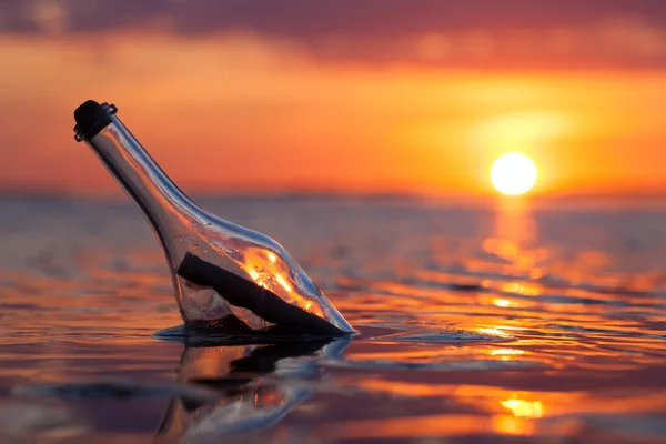 Bouteille avec un message dans la mer au coucher du soleil — Photo