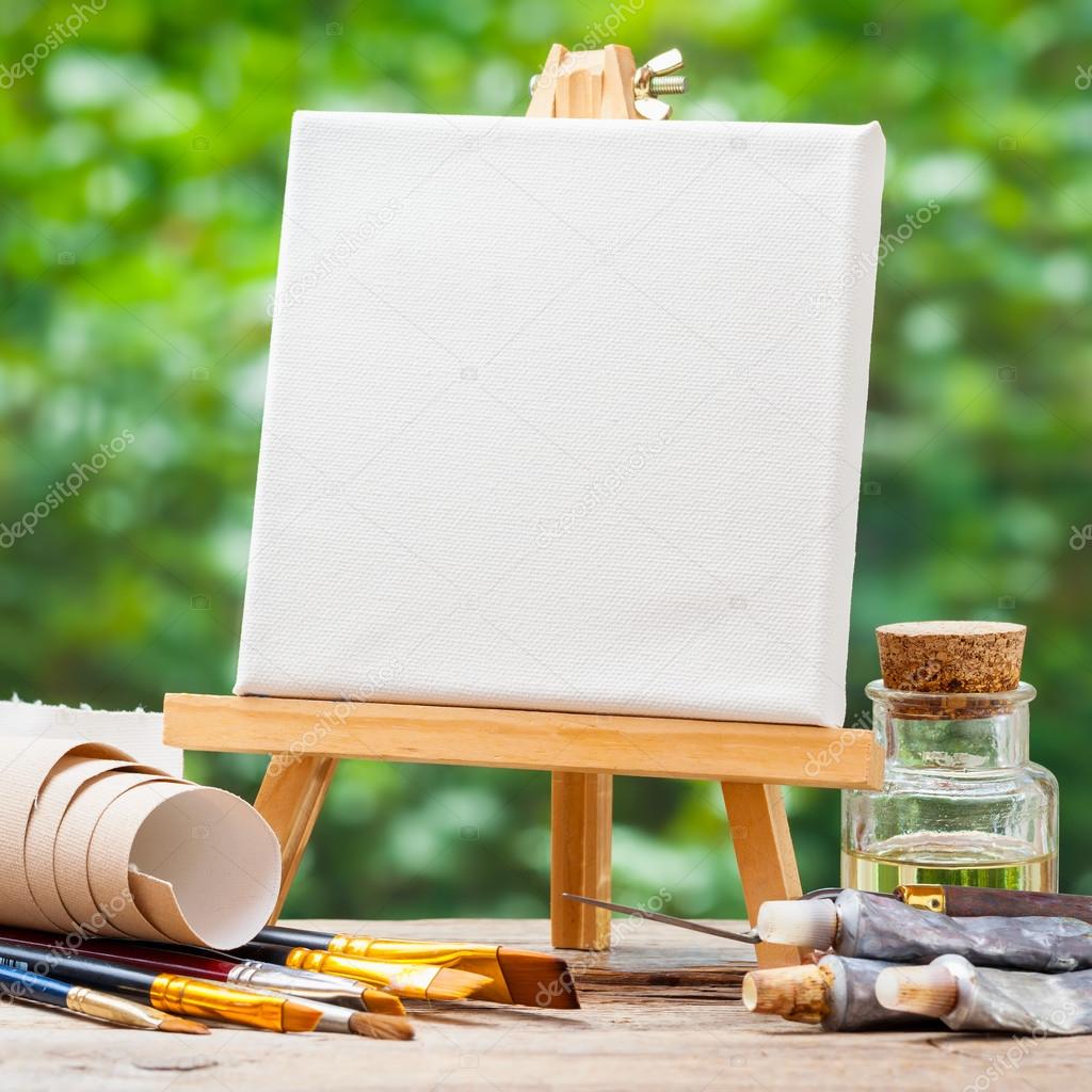 Artist paintbrushes, paint tubes and small easel with canvas