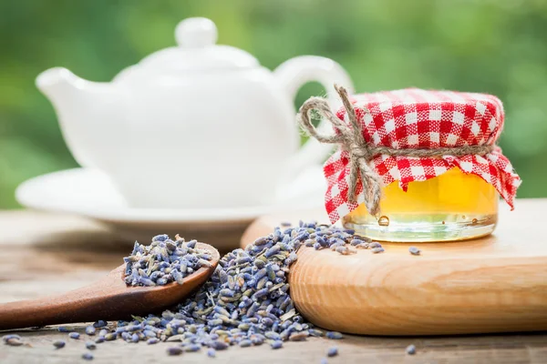 Frasco de mel, chá de lavanda saudável seco e bule de chá no fundo . — Fotografia de Stock