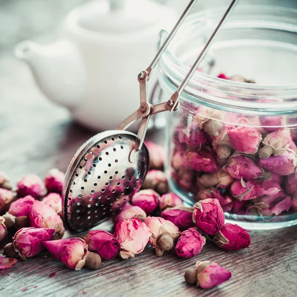 Rose brotes de té, infusor de té, tarro de vidrio y tetera en el fondo . —  Fotos de Stock